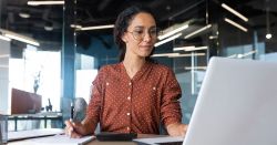 Woman  doing research at a laptop and taking notes on a notepad